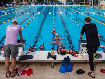 Trening na 50-metrowym basenie, dwoje trenerów przy słupkach startowych