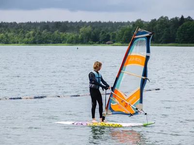 Uczestnik na desce windsurfingowej stawia żagiel z napisem Junior