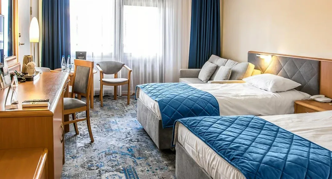 Pokój hotelowy z dwoma łóżkami, biurkiem i fotelem przy oknie