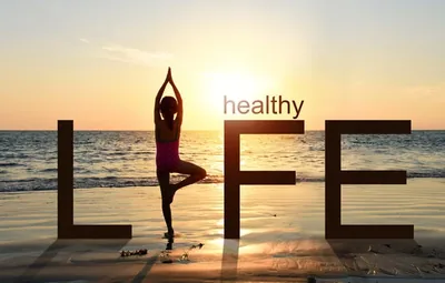 Napis „healthy LIFE” na plaży, w miejscu litery I sylwetka osoby w pozycji drzewa
