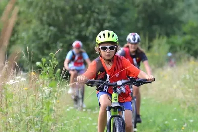 Uczestnik w kasku i okularach jedzie na rowerze łąką, za nim reszta grupy