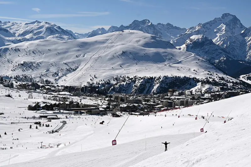 Widok na Alpe d'Huez z ośnieżonego stoku, zabudowa ośrodka na płaskowyżu, w tle ośnieżone szczyty