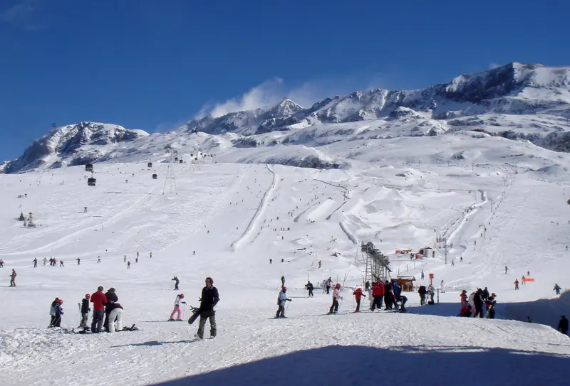 Snowpark w Alpe d'Huez, narciarze na szerokim stoku, w tle ośnieżony grzbiet