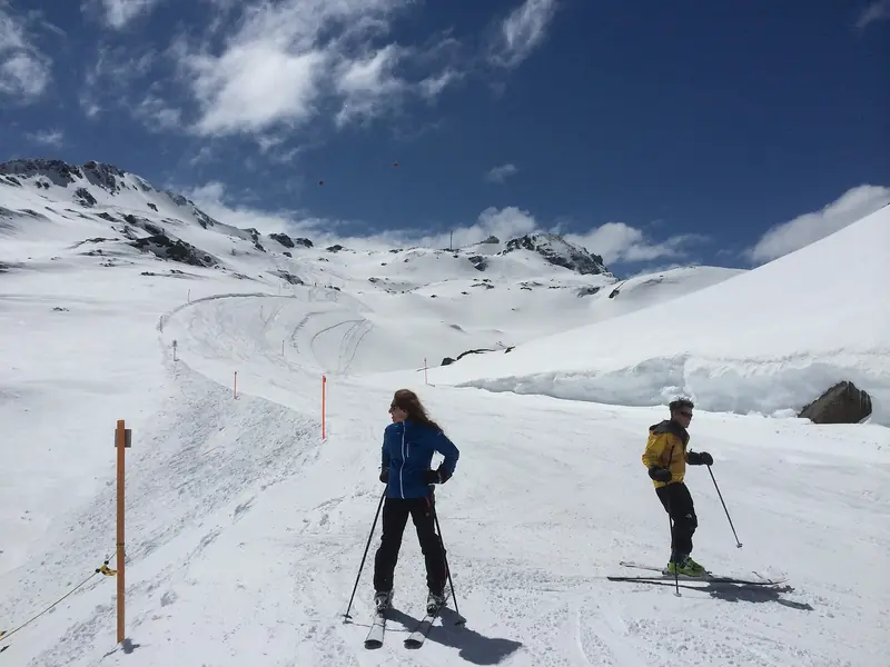 Dwoje narciarzy na trasie pod Parpaner Rothorn, tyczki przy krawędzi, w tle ośnieżone szczyty