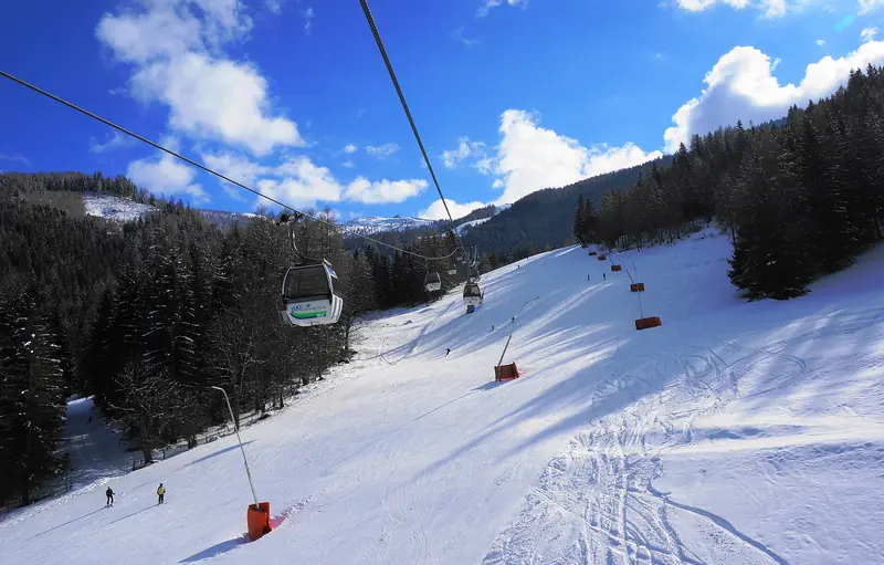 A chairlift above a sunny snowy Bad Kleinkirchheim piste, skiers and the Nockberge forests