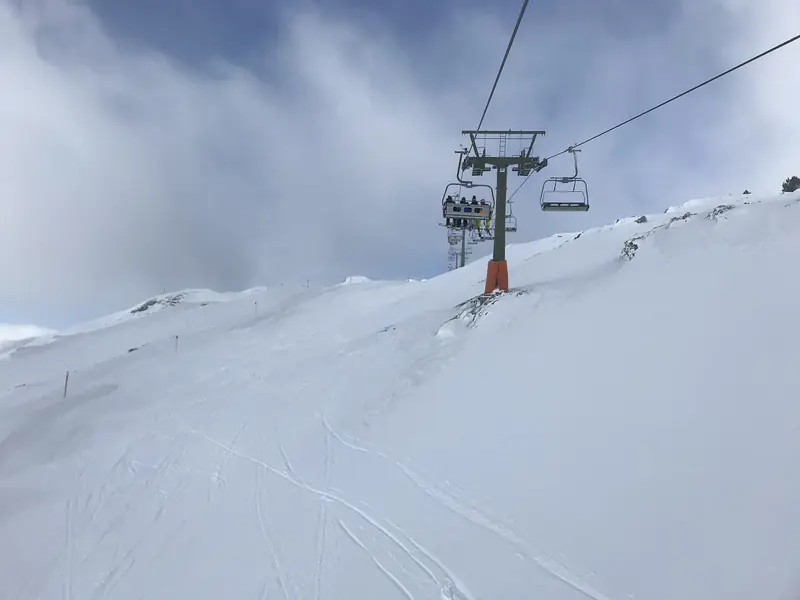A chairlift over a snow-covered Baqueira-Beret slope, ski tracks in the snow and cloud over the ridge