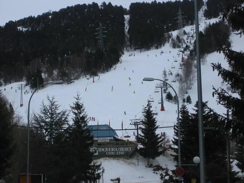The Baqueira-Beret base at 1,500 m: a piste with skiers and a lift among snow-covered spruces