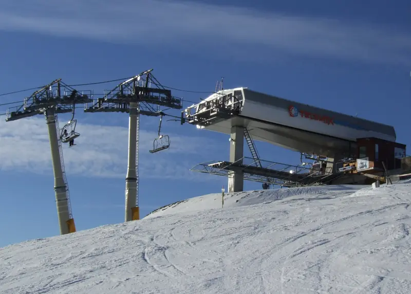 A chairlift top station above a snowy Donovaly piste, ski tracks under a blue sky