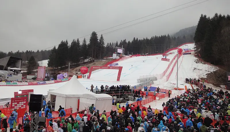 The snowy Kandahar piste at Garmisch-Partenkirchen with the grandstand and crowd during a race, firs on the slope