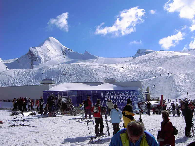 Lodowiec Kitzsteinhorn nad Kaprun: ośnieżony szczyt nad stacją narciarską, narciarze zebrani na śniegu pod błękitnym niebem