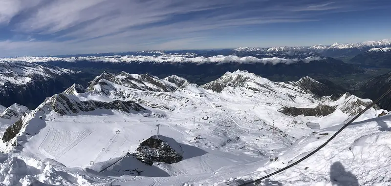 Panorama lodowcowego terenu narciarskiego Kitzsteinhorn ze szczytu, trasy i wyciągi na śniegu, w tle grzbiety Wysokich Taurów
