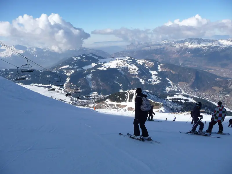 Skiers on the red Aiguille piste at La Clusaz, a chairlift and the village, the Aravis massif behind