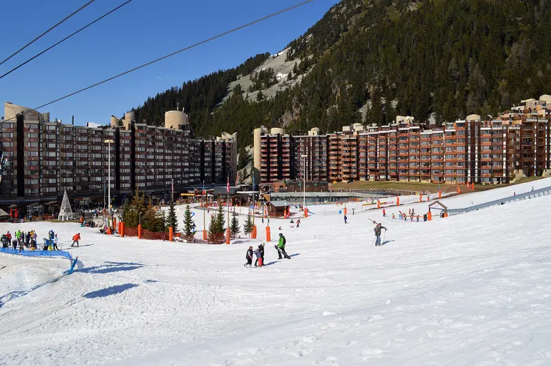 Front śniegu w Plagne Bellecôte: bloki apartamentowe przy stoku i narciarze pod wyciągami