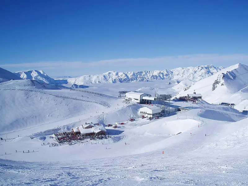 A station and pistes of Les Deux Alpes high above the valley, snowfields reaching to distant ridges