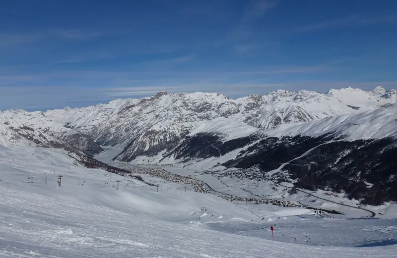 Widok z wyratrakowanej trasy na dolinę Livigno, zabudowa miasteczka wzdłuż drogi, w tle ośnieżone szczyty