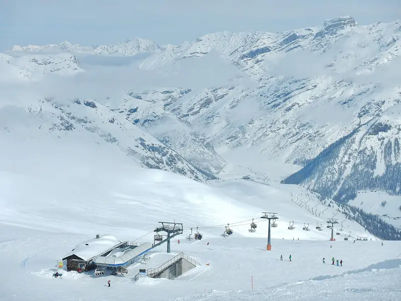 Stacja wyciągu krzesełkowego Costaccia na stoku nad doliną Livigno, narciarze i linia krzesełek