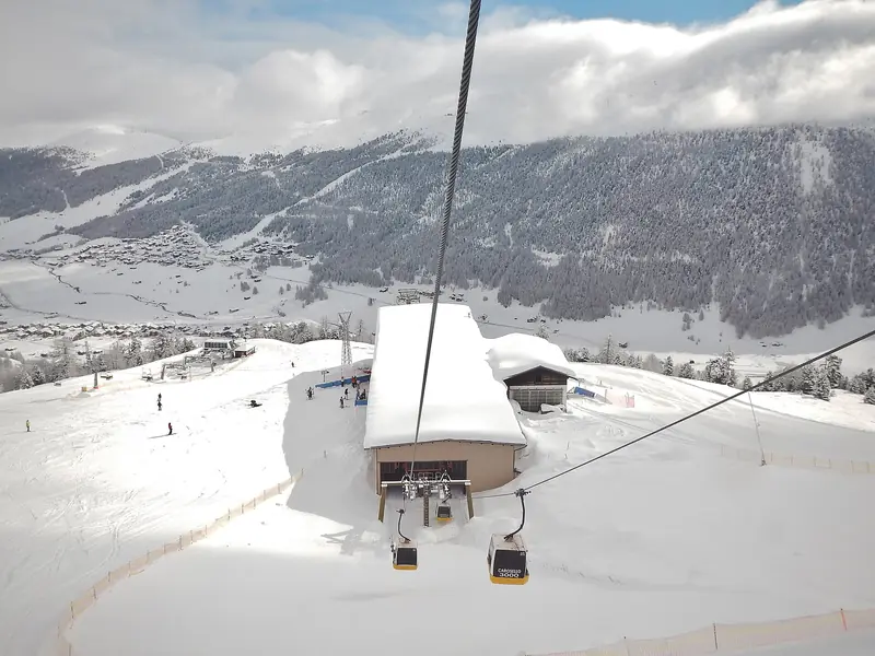 Kabiny gondoli Carosello 3000 nad stacją pośrednią, w dole zabudowa Livigno i zalesione zbocze