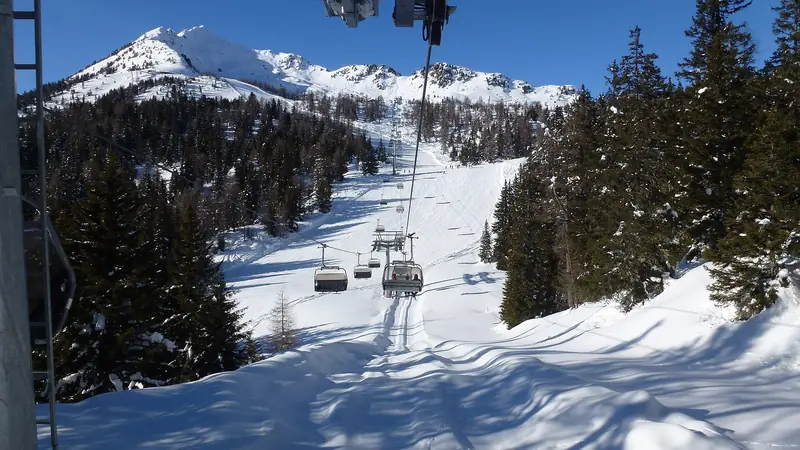 A chairlift above a snowy Madonna di Campiglio piste, a snowy peak behind