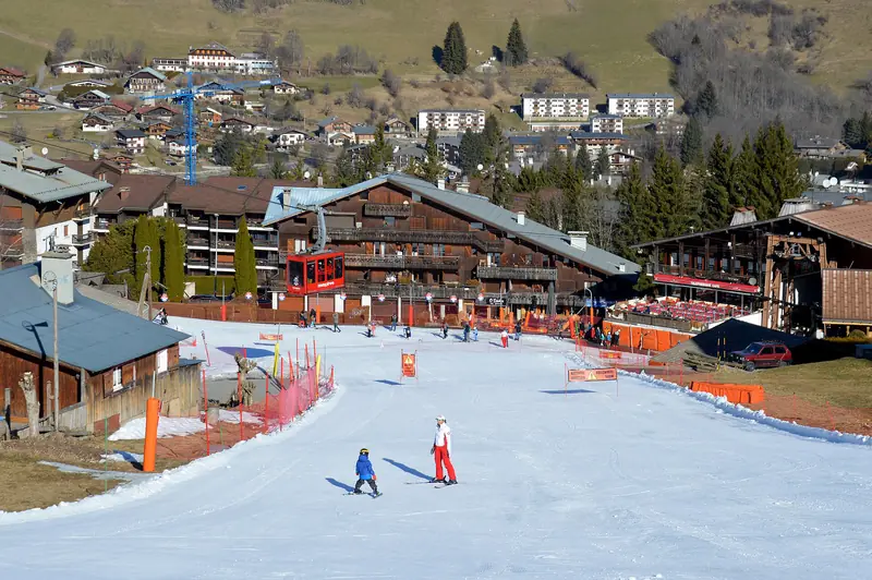 The Rochebrune ski front at Megève: skiers on the piste below timber buildings, a gondola over the slope
