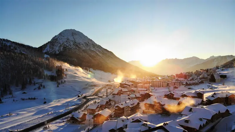 The snow-covered village of Montgenèvre on the border pass at sunrise, a steep peak above the buildings and slopes behind