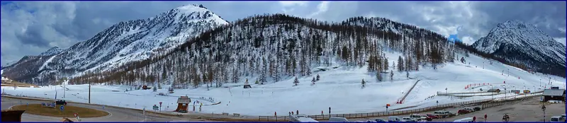 A winter panorama of the Montgenèvre slopes with piste and lift lines, snow-covered flanks under cloud