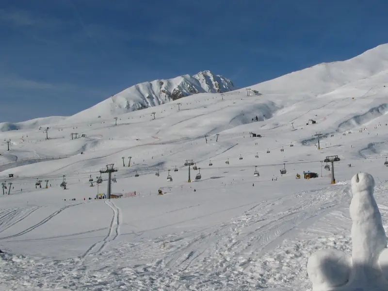 Szeroki, ośnieżony Passo Tonale w słońcu: wachlarz wyciągów krzesełkowych i gondoli wznoszący się po bezleśnym stoku, w tle ośnieżone szczyty