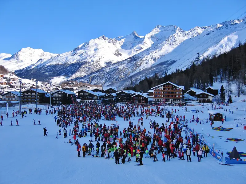 The Saas-Fee base: a crowd of skiers on the snow, the snowy Mischabel massif behind under a blue sky