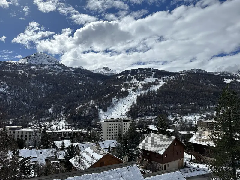 Saint-Chaffrey zimą: ośnieżone dachy wsi, nad nią trasy Serre Chevalier w lesie