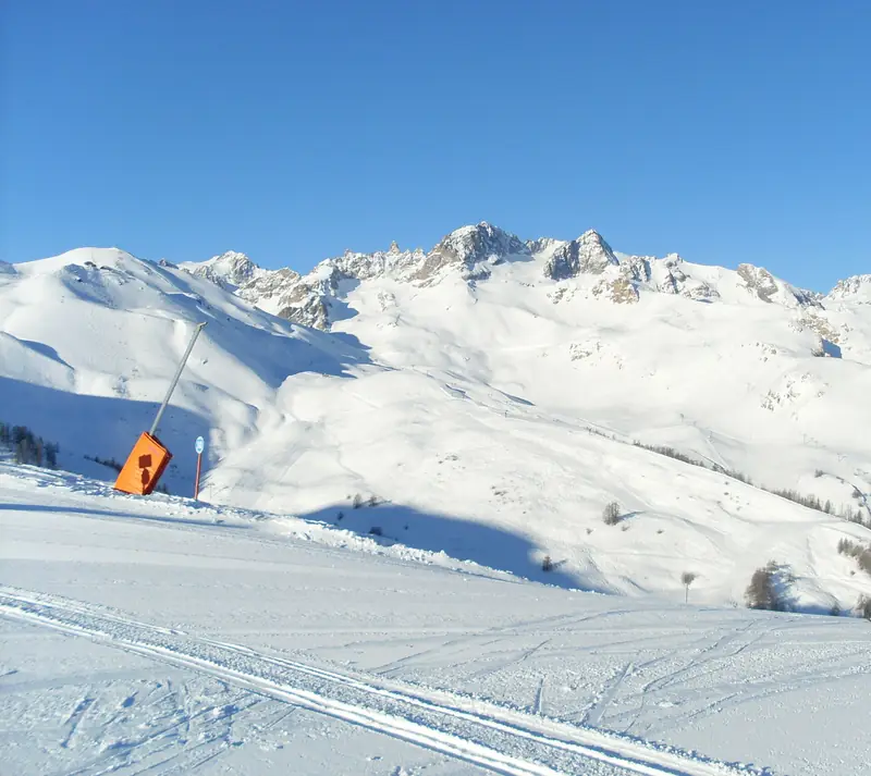 Wyratrakowana trasa w Serre Chevalier, armatka śnieżna przy krawędzi, w tle ośnieżone szczyty