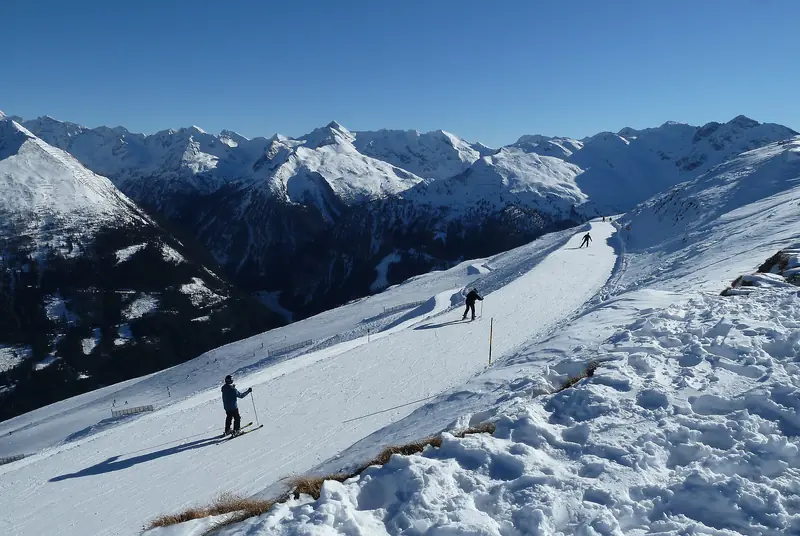 Skiers on a groomed Stubnerkogel piste above Bad Gastein, a wide panorama of snow-covered peaks behind