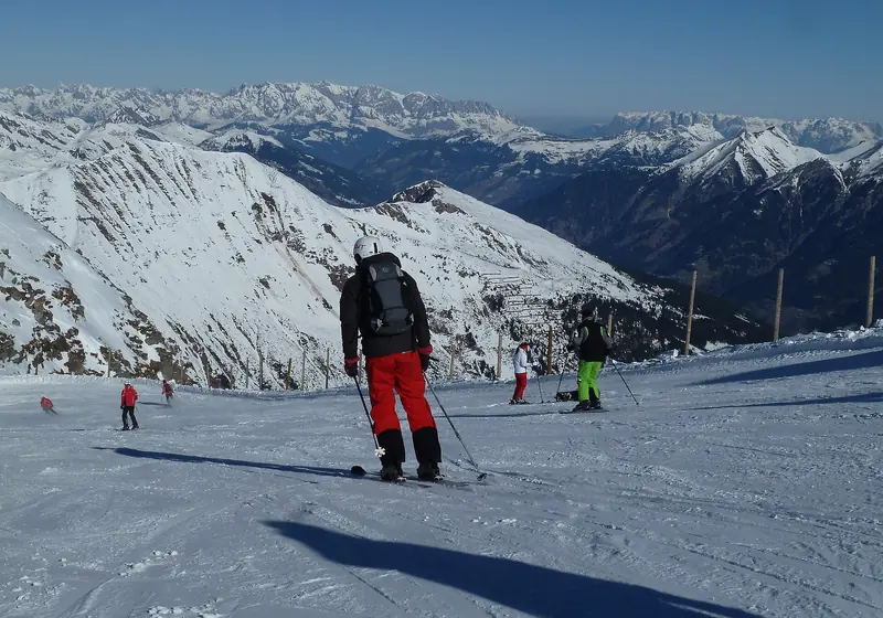 Skiers on the Kreuzkogel slope at Sportgastein, the ridges of the High Tauern behind under a blue sky