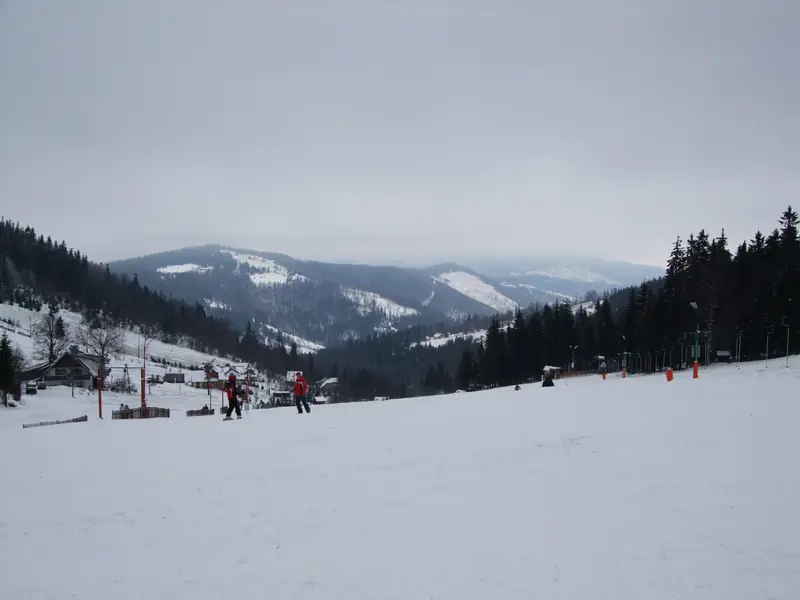 A snowy ski meadow at Szczyrk (Biały Krzyż), skiers and the Beskid ridges behind