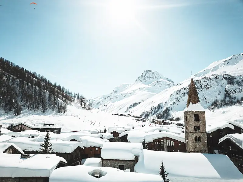 Val d'Isère zimą: ośnieżone dachy i wieża kościoła, w tle stoki ośrodka