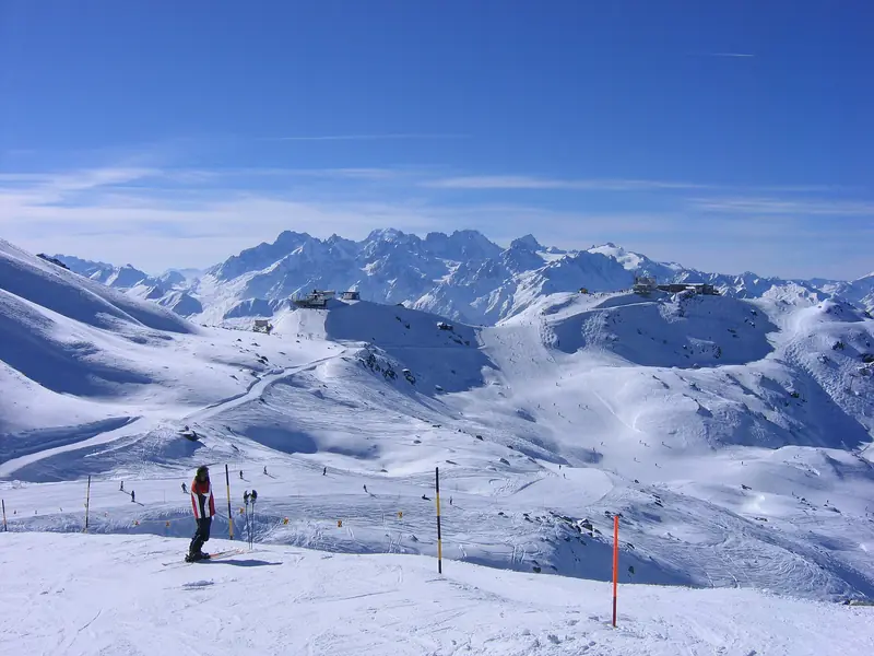 Narciarz na szerokiej trasie w Verbier, tyczki wzdłuż krawędzi, w tle ośnieżone grzbiety