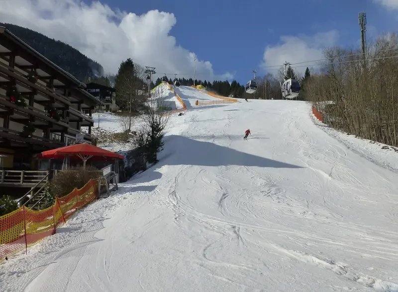 Szeroka trasa Nordabfahrt ze Schmittenhöhe nad Zell am See, narciarz na wyratrakowanym śniegu, gondole i chata przy stoku