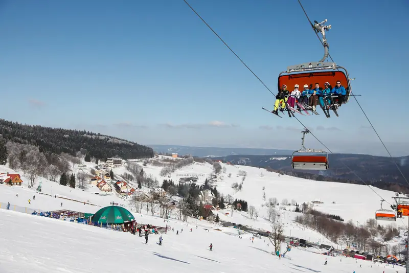 A chairlift with skiers above the snowy base of Zieleniec Ski Arena