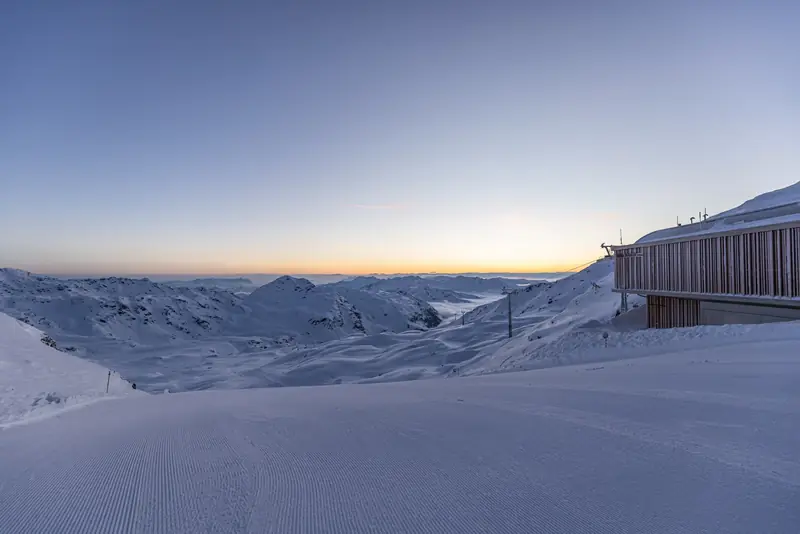 A groomed Zillertal Arena slope at dusk, the top-station building on the right and snowy ridges behind